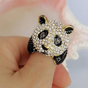 Peut inclure: Une bague dor&eacute;e repr&eacute;sentant un panda. La t&ecirc;te du panda est recouverte de strass transparents &eacute;tincelants avec des accents en &eacute;mail noir autour des yeux et des oreilles. Les pattes du panda sont incrust&eacute;es de petits cristaux noirs sur les c&ocirc;t&eacute;s.