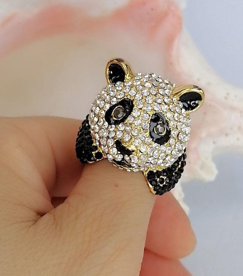 Peut inclure: Une bague dor&eacute;e repr&eacute;sentant un panda. La t&ecirc;te du panda est recouverte de strass transparents &eacute;tincelants avec des accents en &eacute;mail noir autour des yeux et des oreilles. Les pattes du panda sont incrust&eacute;es de petits cristaux noirs sur les c&ocirc;t&eacute;s.