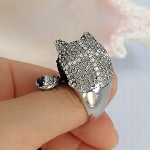 Pu&ograve; includere: Un anello color argento con un design a testa di animale tridimensionale. La superficie superiore &egrave; densamente incrostata di numerosi piccoli cristalli chiari e scintillanti, con un piccolo dettaglio dell'orecchio scuro che sporge dal lato.