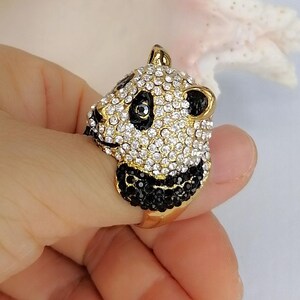 Peut inclure: Une bague dor&eacute;e repr&eacute;sentant une t&ecirc;te de panda en trois dimensions. Le visage du panda est incrust&eacute; de cristaux blancs transparents, tandis que des cristaux noirs forment les yeux, les oreilles et le museau. L'anneau est en m&eacute;tal dor&eacute; lisse.