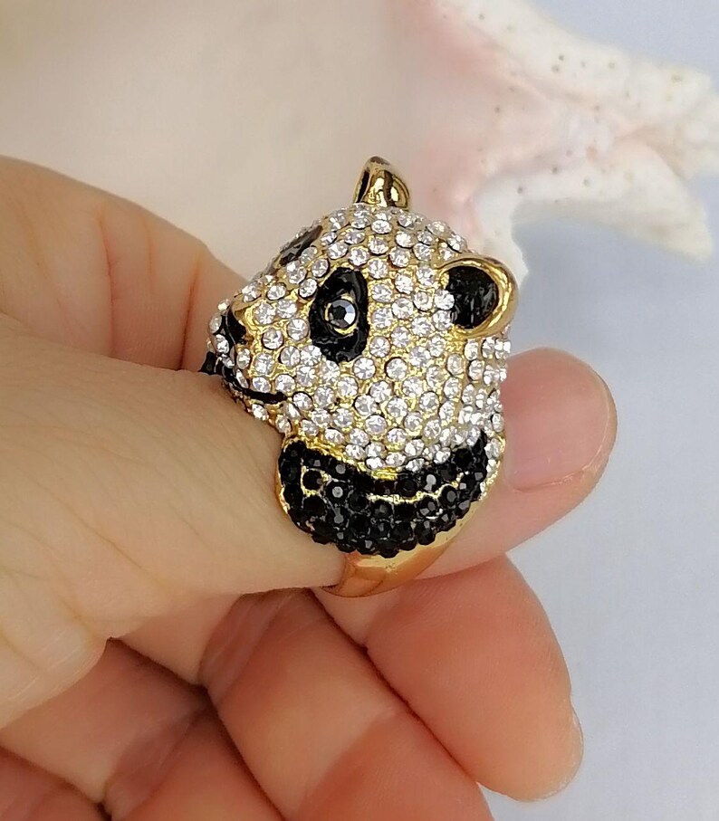 Peut inclure: Une bague dor&eacute;e repr&eacute;sentant une t&ecirc;te de panda en trois dimensions. Le visage du panda est incrust&eacute; de cristaux blancs transparents, tandis que des cristaux noirs forment les yeux, les oreilles et le museau. L'anneau est en m&eacute;tal dor&eacute; lisse.
