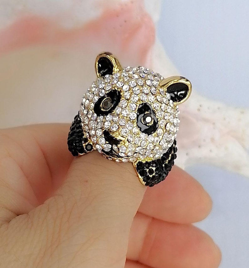 Peut inclure: Une bague en forme de t&ecirc;te de panda, dot&eacute;e d'une base en m&eacute;tal dor&eacute; recouverte de strass blancs transparents. Le panda pr&eacute;sente des accents en &eacute;mail noir autour des yeux, des oreilles et des pattes, avec de petits cristaux noirs incrust&eacute;s.