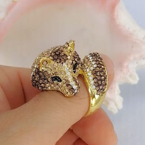 Pu&ograve; includere: Un anello color oro a forma di testa di volpe, interamente incastonato con piccoli cristalli scintillanti marroni, beige e trasparenti. La volpe presenta occhi in cristallo nero e una coda curva che si avvolge per formare il gambo dell'anello.