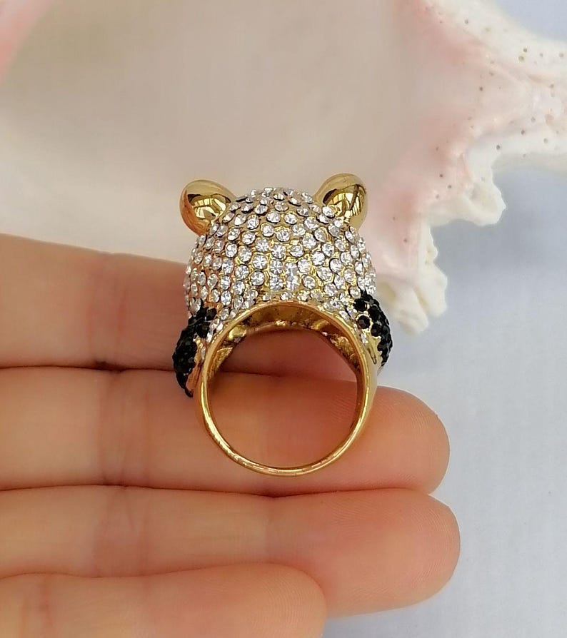 Peut inclure: Une bague dor&eacute;e en forme de t&ecirc;te de panda, dot&eacute;e d'un anneau et d'oreilles en m&eacute;tal dor&eacute; poli. Le sommet de la t&ecirc;te est recouvert de strass blancs transparents, tandis que les oreilles et le contour des yeux sont orn&eacute;s de petits strass noirs.
