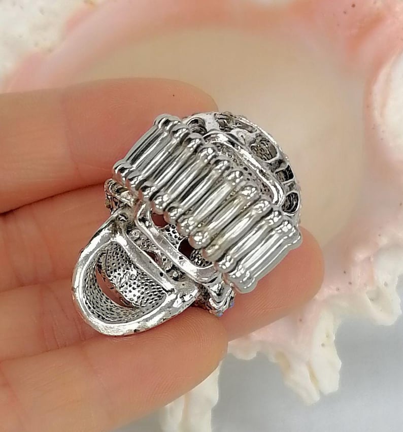 May include: A silver-toned ring featuring a wide, flexible band constructed from multiple vertical metal bars. The ring has a textured, open-work design with a metallic finish, showcasing a structured, cage-like appearance across the entire surface.