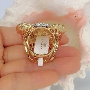 May include: A gold-toned ring featuring a bear-shaped head adorned with clear crystals. The metal surface has a textured finish, and a white rectangular tag with the printed text 00208 is attached to the inner band of the ring.