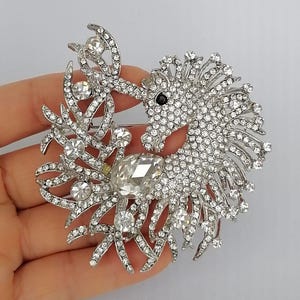 May include: A silver-toned brooch in the shape of a seahorse, encrusted with clear crystals. The seahorse has a black eye and is surrounded by crystal-studded foliage. A large, teardrop-shaped crystal is at the center of the design.