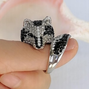 Pu&ograve; includere: Un anello color argento con un design a testa di volpe incastonato con strass neri e trasparenti. La testa della volpe &egrave; posizionata sulla parte superiore, mentre la fascia dell'anello si estende a formare una coda curva, anch'essa decorata con strass neri e trasparenti.