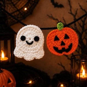 May include: A crochet garland featuring a white ghost with black eyes and a mouth, and an orange pumpkin with a green stem and a black jack-o'-lantern face, both suspended from a black cord against a dark, festive Halloween-themed background.