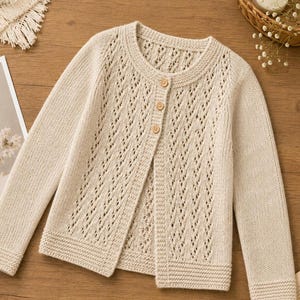 Può includere: Un cardigan in maglia beige a maniche lunghe con un delicato motivo a rombi traforati sui pannelli frontali. Il capo presenta uno scollo rotondo, polsini e orlo a coste, ed è chiuso da tre piccoli bottoni rotondi in legno chiaro.