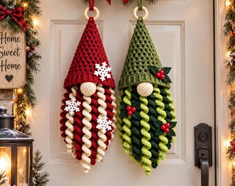 May include: Two hanging crochet gnome decorations with pointed hats and long curly beards. One gnome features a red hat with white snowflake accents, while the other has a green hat with holly leaf and red berry embellishments on a wooden ring.