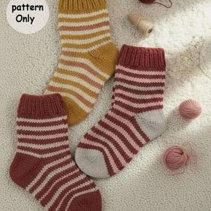 May include: Three knitted socks with ribbed cuffs and horizontal stripes in mustard yellow, maroon, and light grey. The socks are arranged with small balls of yarn. A circular white label in the upper left corner contains the text pattern Only.