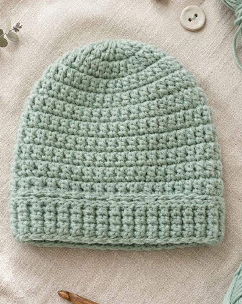 May include: A light green, handmade crochet beanie hat. The hat is made of soft yarn and features a ribbed brim and a textured stitch pattern. The hat is a solid color and appears to be new.