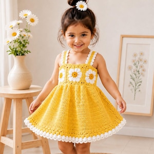 May include: A yellow crochet dress featuring a bodice adorned with white and yellow daisy motifs, thick straps, and a flared skirt with a white scalloped hem. The dress is paired with a matching white daisy hair accessory.