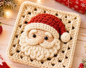 May include: A square crochet granny square featuring a three-dimensional Santa Claus face in the center. The Santa has a red hat with a white pom-pom, a beige face, black bead eyes, and a textured white beard and mustache made of yarn.
