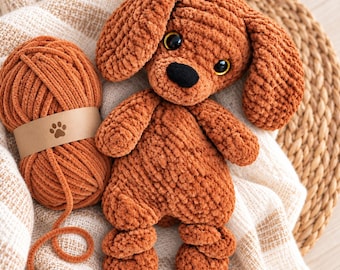 May include: A brown crochet dog plush toy with large floppy ears and black plastic eyes, positioned next to a matching ball of soft brown yarn wrapped in a paper band featuring a small brown paw print icon on the front of the label.