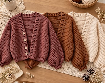 May include: Three long-sleeved, chunky knit cardigans in mauve, brown, and cream. Each cardigan features a V-neckline, ribbed cuffs, and a front button closure with four light-colored circular buttons on the mauve piece.