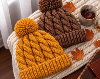 May include: Two knit beanies with pom-poms, one in mustard yellow and one in dark brown. Both hats feature a thick cable knit pattern and a wide ribbed cuff. The beanies are crafted from yarn and display a textured, chunky knit construction.