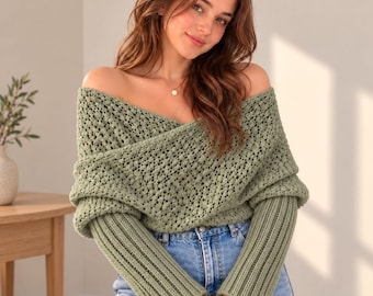 May include: An off-the-shoulder sage green sweater featuring a textured, open-knit crossover bodice and long, ribbed sleeves. The garment is paired with light blue denim jeans, creating a cohesive look with a soft, muted color palette.