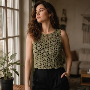 May include: A sleeveless olive green crochet top featuring an intricate openwork shell stitch pattern, a round neckline, and a cropped silhouette, paired with black trousers. The garment is constructed with a textured yarn in a repeating fan design.