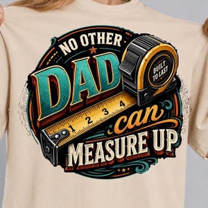 May include: A beige t-shirt featuring a circular graphic with a yellow and black tape measure. The text reads NO OTHER DAD can MEASURE UP and BUILT TO LAST. The design uses teal, orange, and black colours with a vintage-inspired aesthetic.