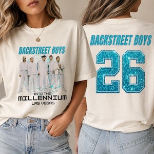 Könnte beinhalten: Ein cremefarbenes T-Shirt mit einer Grafik der Backstreet Boys in weißen Outfits, dem Text Backstreet Boys Into The Millennium Las Vegas auf der Vorderseite und dem Text Backstreet Boys mit der Zahl 26 in blauem Glitzer auf der Rückseite.