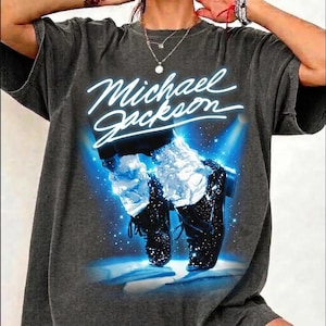 May include: Dark gray t-shirt featuring a graphic of Michael Jackson's iconic dance pose. The image shows black shoes, white socks, and a blue spotlight effect. The text "Michael Jackson" is written in white script across the top.