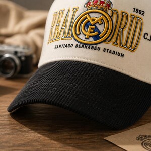 Pu&ograve; includere: Cappellino da baseball color crema con visiera nera, con il logo e il testo del Real Madrid. Il cappellino presenta ricami dorati e blu, con le parole "REAL MADRID" e "SANTIAGO BERNABEU STADIUM". L'anno "1902" &egrave; anch'esso ricamato.