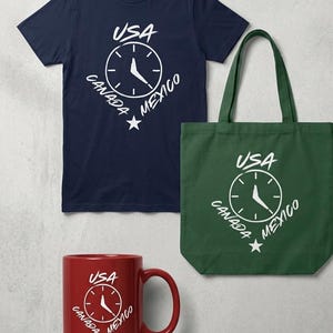 Puede incluir: Una camiseta azul marino, una bolsa de mano verde y una taza roja, cada una con un diseño de reloj blanco con el texto "USA CANADA MEXICO". El diseño incluye una estrella. Los artículos son probablemente temáticos de viajes o recuerdos.