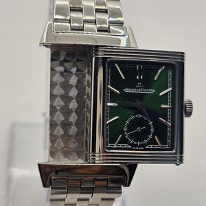 Puede incluir: Un reloj de pulsera rectangular plateado con esfera verde efecto rayos de sol, que muestra el logotipo y el texto de Jaeger-LeCoultre. El reloj tiene una correa de eslabones metálicos, un subdial para segundos y una caja giratoria con textura.