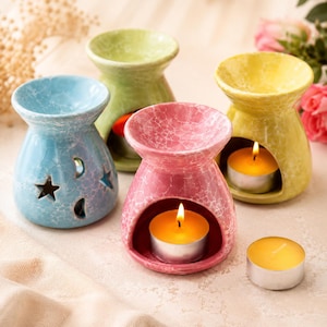 May include: Four ceramic essential oil diffusers in blue, green, pink, and yellow. The blue diffuser has star and moon cutouts. The pink and yellow diffusers have lit candles inside. The diffusers have a crackle glaze finish.
