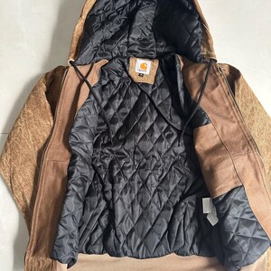 May include: A brown hooded jacket with a black quilted lining. The jacket has a zipper closure and a brown exterior with a textured appearance. The interior lining is black and quilted. The jacket has a tag with a logo.
