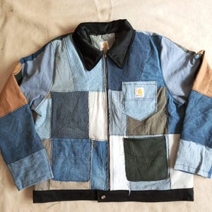 Puede incluir: Una chaqueta de patchwork confeccionada con varios tonos de mezclilla azul, tela color canela y paneles verde oliva. La chaqueta presenta un cuello negro, un dobladillo inferior negro, cierre de cremallera frontal y un bolsillo con etiqueta Carhartt.