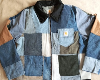 May include: A patchwork jacket constructed from various shades of blue denim, tan fabric, and olive green panels. The jacket features a black collar, a black bottom hem, a front zipper closure, and a chest pocket with a Carhartt brand label.
