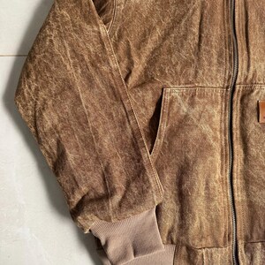 May include: Brown jacket with a full-length zipper, a front pocket, and a ribbed cuff. The jacket has a worn, textured appearance. The jacket is a medium brown color.