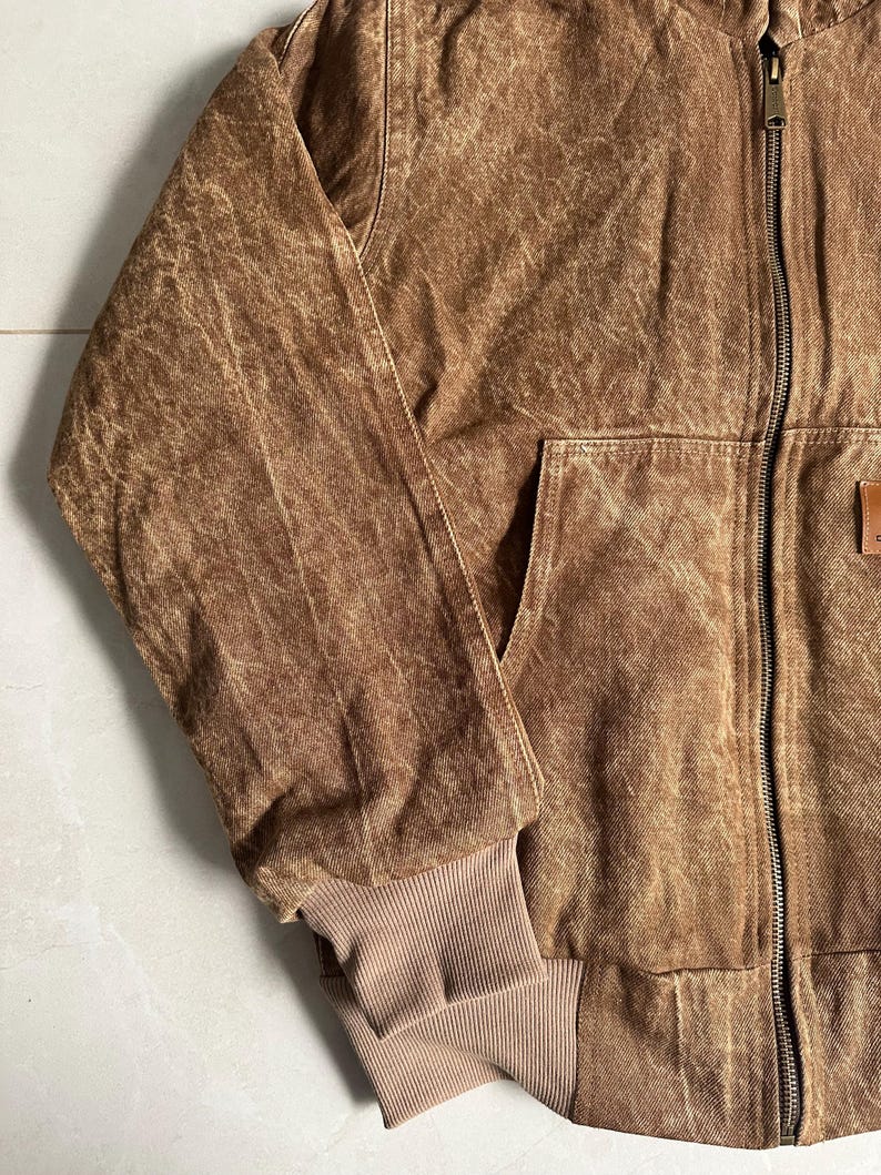 May include: Brown jacket with a full-length zipper, a front pocket, and a ribbed cuff. The jacket has a worn, textured appearance. The jacket is a medium brown color.