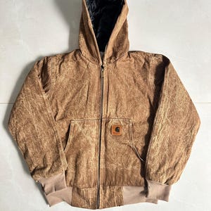 May include: Brown hooded jacket with a zip-up front, a front pocket, and ribbed cuffs and hem. The jacket features a small square logo patch on the front. The interior lining of the hood is black.