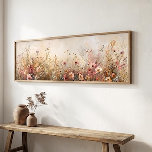 Puede incluir: Una pieza de arte mural rectangular y alargada con un marco que muestra una pintura impresionista de un campo de flores silvestres en tonos suaves de rosa, naranja y crema. La obra cuelga sobre un banco de madera con dos jarrones de cerámica marrón.
