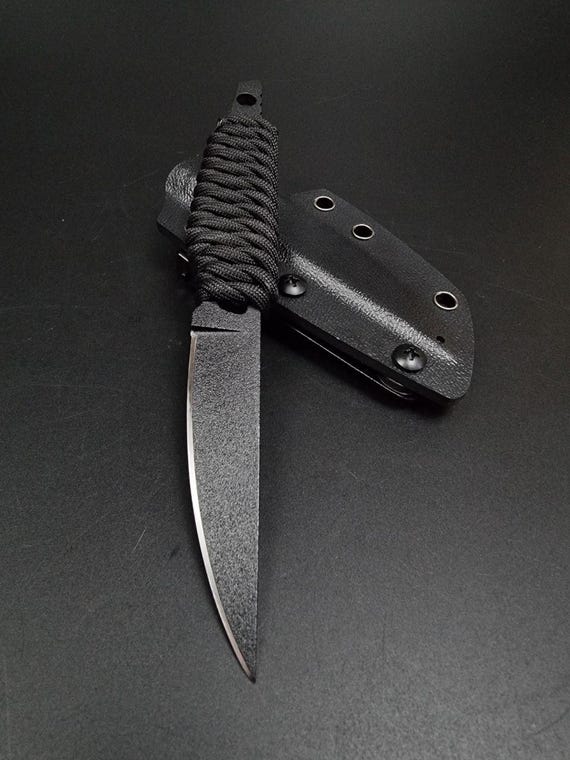 A slim, hand-forged bushcraft knife with black paracord wrap — clearly made by a bladesmith with a distinct aesthetic, not a factory.