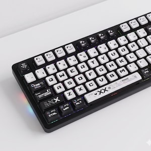 Könnte beinhalten: Eine schwarze mechanische Tastatur mit weißen Tastenkappen und schwarzen Akzenten. Die Tastatur verfügt über ein Standard-QWERTZ-Layout mit Funktionstasten und einer Leertaste. Die Tasten haben verschiedene Symbole und Texte, darunter "PRINT" und "XX".
