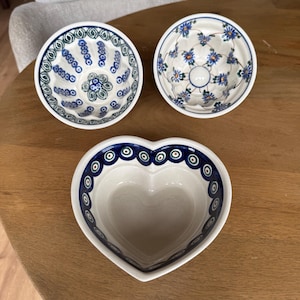 May include: Three ceramic bowls with hand-painted patterns. Two bowls are round with fluted sides, one featuring blue and green floral motifs and the other blue flowers. The third bowl is heart-shaped with a blue and green circular rim pattern.
