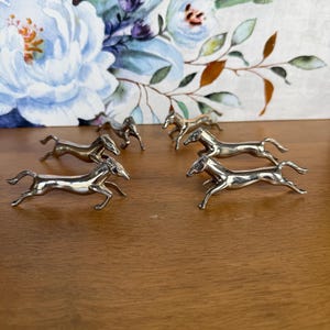 Op de afbeelding: Een set van vier kleine, gepolijste zilverkleurige metalen paardenbeeldjes in een dynamische rennende houding. Elk paard is vervaardigd met gladde, reflecterende oppervlakken en gedetailleerde manen, staarten en benen voor een actieve uitstraling.