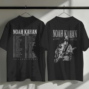 Può includere: Due magliette nere con la scritta "NOAH KAHAN 2026 TOUR". Una maglietta mostra una grafica di Noah Kahan che suona la chitarra, l'altra elenca le date del tour. Entrambe sono appese a una gruccia nera.