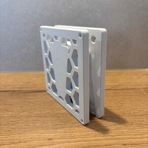 Könnte beinhalten: Ein weißes, quadratisches Objekt mit einem geometrischen Wabenmuster und dem geprägten Wort "HALKARD". Das Objekt besteht aus einem festen Material und hat ein sauberes, modernes Design. Es liegt auf einer Holzoberfläche. Maße: ca. 10 cm x 10 cm.