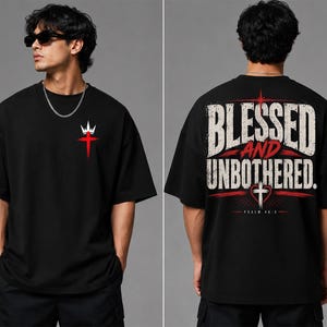 May include: A black short-sleeve t-shirt featuring a small white crown and red cross graphic on the front chest. The back displays the text BLESSED AND UNBOTHERED in large white letters with a red cross, heart, and the text PSALM 46:5 below.