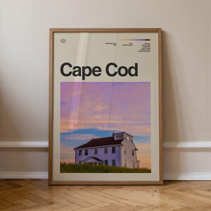 Puede incluir: Un póster enmarcado con las palabras "Cape Cod" en letras negras en negrita. El póster presenta una casa blanca con un tejado marrón sobre un cielo colorido al atardecer. Se incluyen detalles de la ubicación.