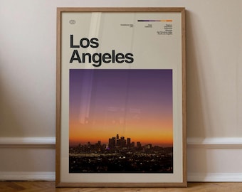 May include: A framed art print featuring the city of Los Angeles at sunset. The print has a beige background with the words "Los Angeles" in bold black letters. The image below shows the city skyline with a purple and orange gradient sky.