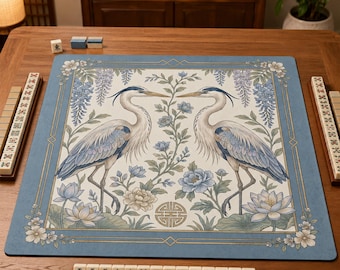 May include: A rectangular mahjong mat featuring a blue border with white floral accents and a central illustration of two grey and blue herons facing each other amidst blue flowers and green vines, with a gold geometric symbol at the bottom centre.