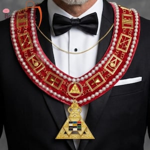 Könnte beinhalten: Ein rotes und goldenes zeremonielles Halsband mit einem dreieckigen Anhänger. Das Halsband hat goldene rechteckige Designs, Perlen und eine goldene Kette. Der Anhänger hat eine dreieckige Form mit bunten Quadraten und goldenen Akzenten. Die Person trägt eine schwarze Fliege und einen Anzug.
