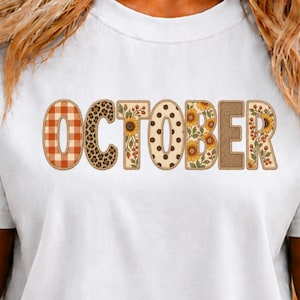 May include: A white t-shirt featuring the word OCTOBER in large block letters. Each letter has a unique pattern: orange plaid, leopard print, sunflowers with berries, brown polka dots, yellow sunflowers, solid brown, and sunflowers with berries.